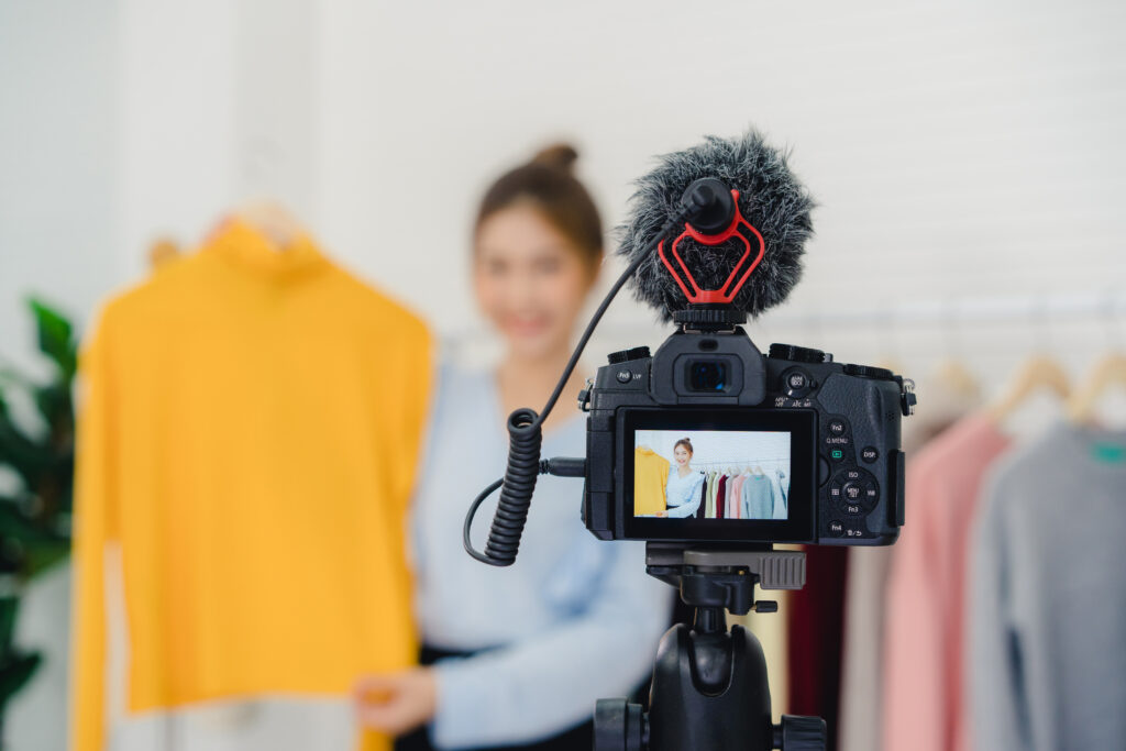blogerka modowa, influencerka internetowa, trzymająca ubranie na wieszaku, nagrywająca nowy film o modzie i transmitująca go na żywo w sieci społecznościowej przez Internet w swoim domu.